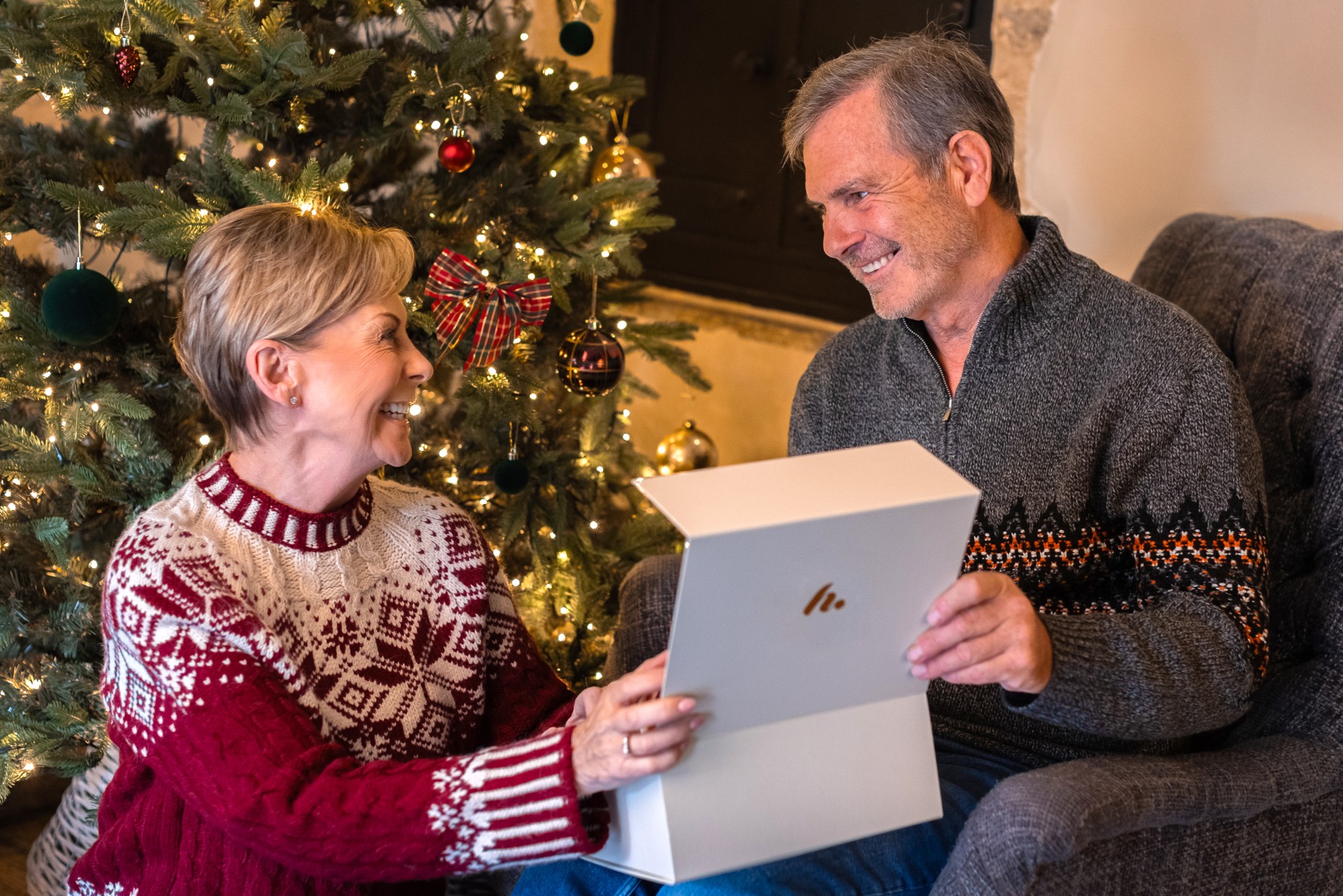 Couple in front of a Christmas tree opening a hampers gift box and smiling