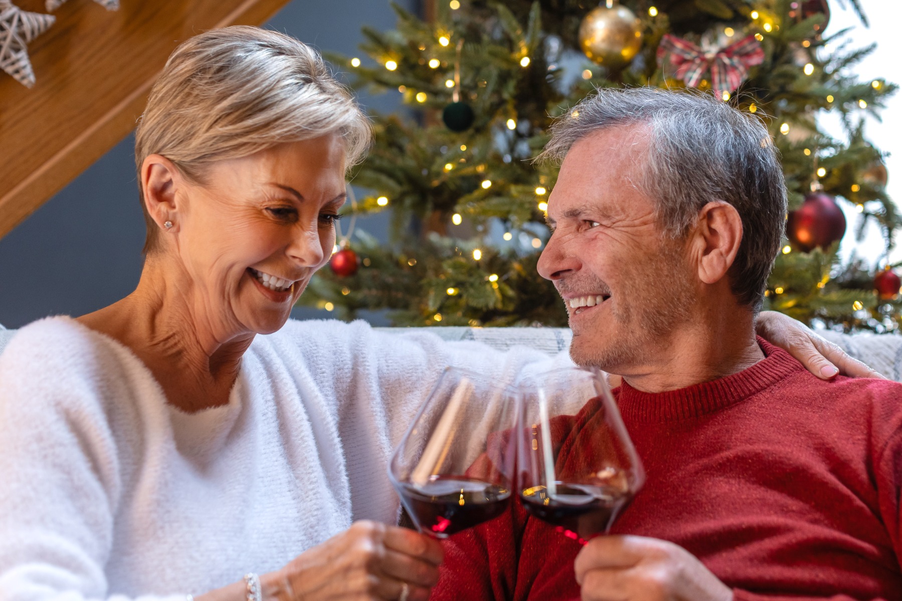 Couple sharing a glass of red wine from a Christmas hamper with a Christmas tree in the background