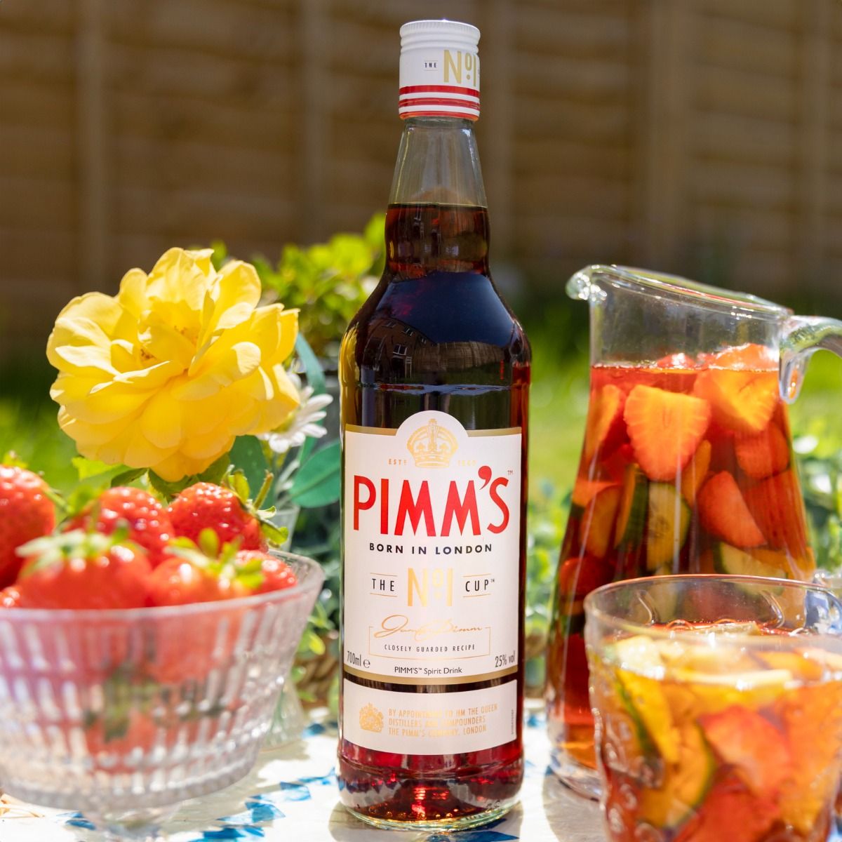 Bottle of Pimms on a table in garden with a drink a glass of Pimm's punch next to it